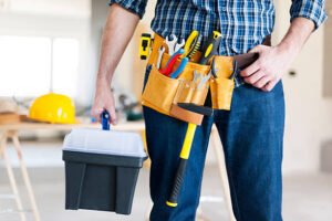 A man stands confidently, holding a tool belt and a toolbox, ready for a construction or repair task, representing affordable handyman services near you.