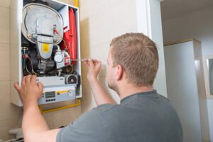 A man repairs a gas boiler in a bathroom, focused on the task with tools and equipment nearby, related to electrical and plumbing troubleshooting.