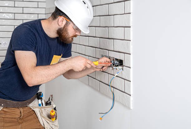 A man wearing a hard hat and safety glasses is diligently working on a wall, performing electrical troubleshooting in Phoenix homes with safety and precision.