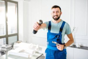A man wearing blue overalls holds a wrench, standing confidently with a focused expression, representing experienced handyman services.