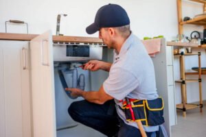 A man repairs a kitchen sink, focused on fixing plumbing issues with tools in hand, representing the best handyman service in Scottsdale.