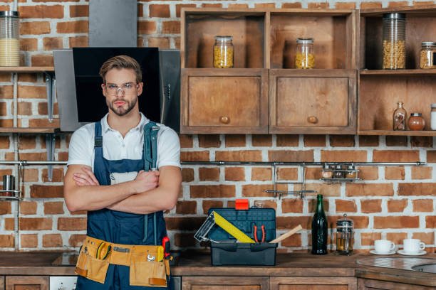 A man wearing overalls stands confidently in front of a textured brick wall, representing the best handyman service in Scottsdale.