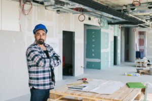 A man stands in an office surrounded by various construction materials, indicating a renovation or building project by a local handyman.
