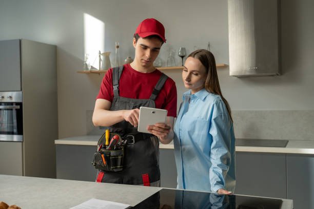 A man and woman in a kitchen, engaged in conversation while looking at a tablet together, discussing plumbing troubleshooting tips.