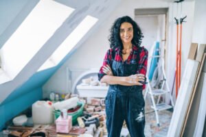 Woman in overalls inspecting drywall damage in an attic for drywall repair near me in Tucson.