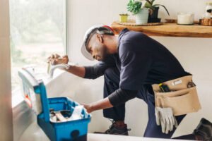 A man is engaged in fixing a sink in a bathroom, performing emergency plumbing service in Phoenix, surrounded by tools and plumbing parts.