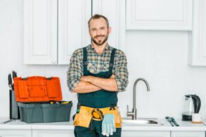 A man wearing overalls stands in a commercial kitchen in Phoenix, representing emergency plumbing services with a confident smile.