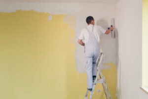 A painting contractor in Tucson, AZ using a roller to apply bright yellow paint to a room, focused on achieving smooth coverage.